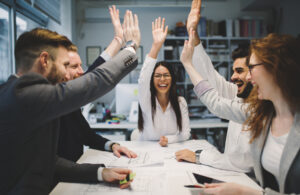 A work team at a desk high fiving each other