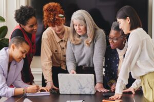 A team of females all looking at a laptop on a desk