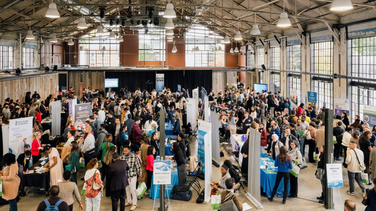 A large job fair inside the Horticulture Building at Lansdowne Park, showing hundreds of job seekers interacting with employer booths along long aisles.