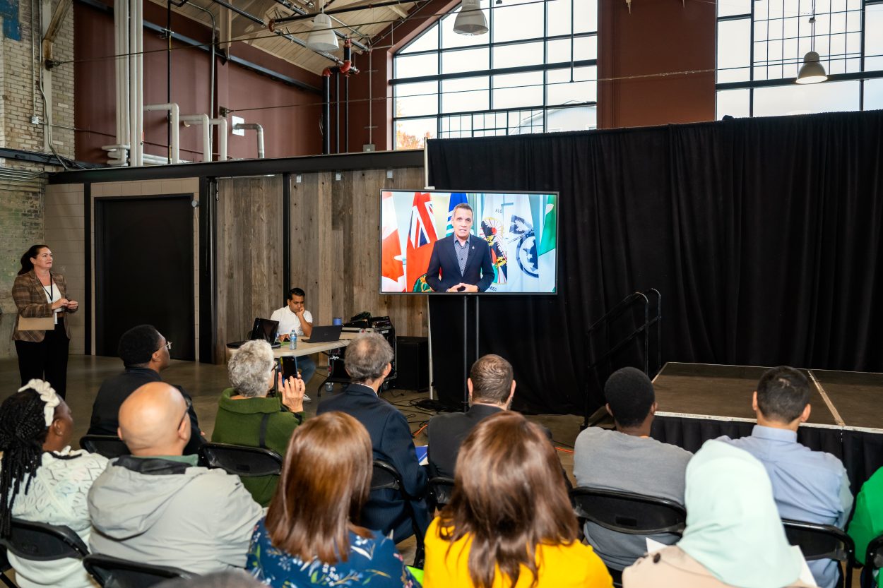 Audience members watch a large screen showing Ottawa's Mayor Mark Sutcliffe, a virtual speaker delivering remarks during the World Skills Job Fair.