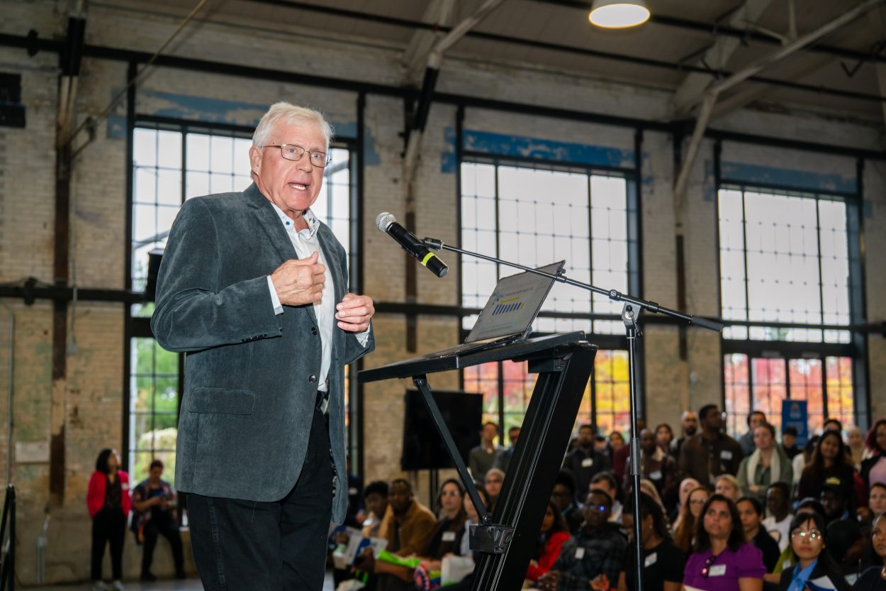 Ian Lee, keynote speaker stands at a podium addressing attendees during the World Skills Job Fair, with a large audience seated behind him.