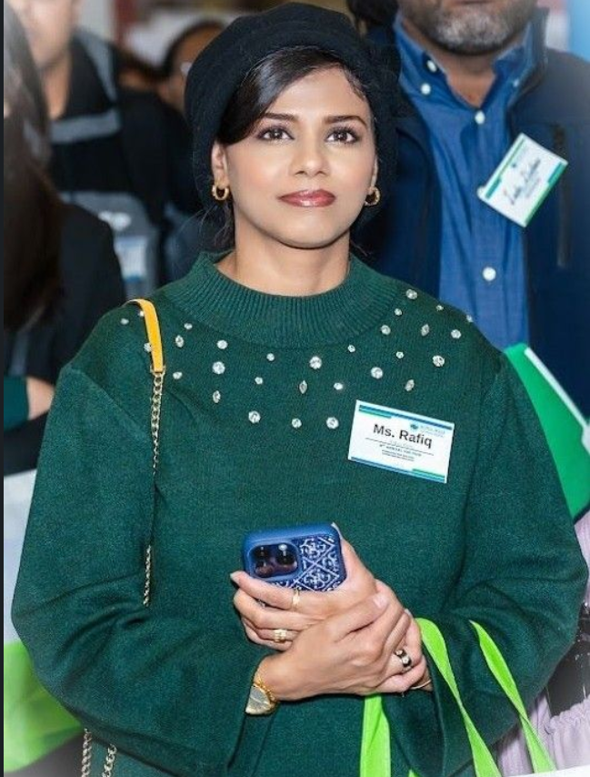 A woman attending the World Skills Job Fair stands holding her phone and event materials, wearing a name badge and looking ahead attentively.